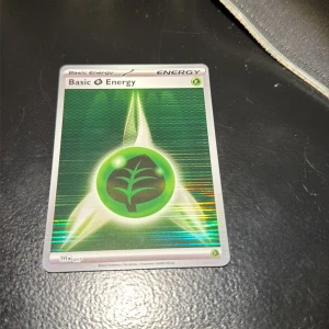 Basic Grass Energy - Cool och glänsande Basic Grass Energy-kort från Pokémon TCG! Perfekt för dig som vill boosta din lek med extra energi och gillar samlarkort. Kortet har en snygg grön design med ett löv, och passar både samlare och spelare som vill sticka ut.