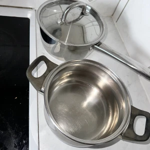 Två rostfria kastruller - Två rostfria kastruller i gott begagnat skick, en med lock och lång handtag, den andra med två grepp. Några mindre repor och tecken på användning syns, men båda är funktionella och passar utmärkt för matlagning. Perfekt för köket och dagligt bruk.