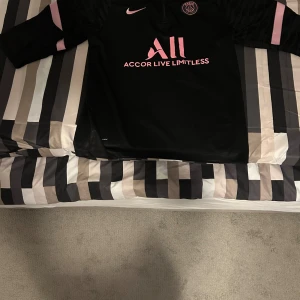 Psg kofta  - Säljer en helt ny svart långärmad Paris Saint-Germain fotbollströja från Nike med rosa detaljer och logga. Tröjan har halv dragkedja fram, Materialet är lätt och andas, perfekt för träning eller match eller bara allmänt streetwear . Storlek L, pris kan diskuteras så tveka inte på att höra av er. 