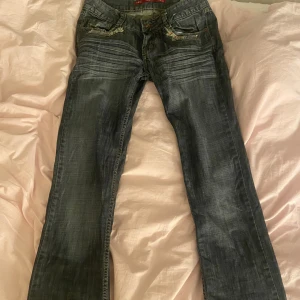 Mörkblå bootcut jeans med slitningar - Snygga mörkblå jeans med bootcut passform och slitna detaljer på fickorna. Jeansen har klassisk femficksdesign, låg midja och coola slitningar framtill och baktill. Jag säljer de för att de är lite för långa för mig.