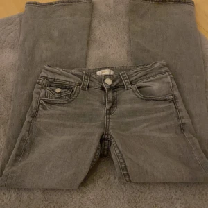 Gråa bootcut  jeans från Gina Tricot - Säljer ett par grå jeansbyxor från Gina Tricot med snygga detaljer som ficklock med knapp både fram och bak. Byxorna har klassisk femficksdesign, bälteshällor  Perfekta för dig som gillar en stilren look med lite edge. Pris kan diskuteras 