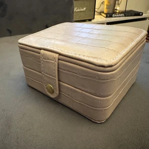 Smyckeskrin | Beige smyckesväska med spegel - Snygg beige smyckeskrin med krokopräglad yta och praktisk spegel i locket. Väskan har flera fack för ringar, örhängen och andra smycken, samt ett guldfärgat tryckknappslås. Perfekt för att hålla koll på dina favoritsmycken.