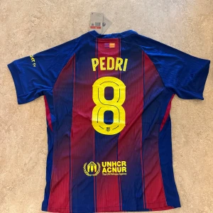 FC Barcelona Pedri matchtröja Nike - Barças officiella matchtröja med Pedri 8 på ryggen. Klassisk randig design i blått och rött, med gula detaljer och klubbmärke på bröstet. Tillverkad i lätt, ventilerande funktionsmaterial. Spotify-logga på framsidan och UNHCR-tryck bak.