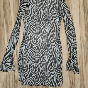 Zebramönstrad meshklänning med lång ärm - Säljer en kort zebramönstrad klänning från H&M i tunn mesh. Klänningen har lång ärm, hög hals och figurnära passform. Svart och vit färg med transparent material som ger en edgy vibe. Perfekt för dig som gillar att sticka ut med djurmönster.