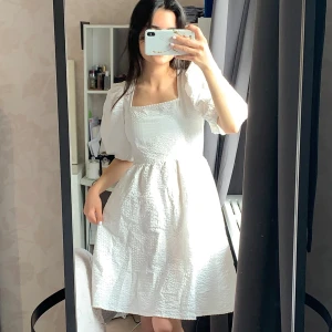 Vit kortklänning från Holly & Whyte (min student klänning)  - Superfin vit klänning från Holly & Whyte med puffiga kortärmar och fyrkantig urringning. Klänningen har en strukturerad, bubblig yta och är lätt utställd i kjolen. Perfekt för sommarens alla tillfällen, riktigt söt och trendig modell. DEN HAR INGA MÄRKEN FRÅN STUDENTEN PLUS DEN HAR FICKOR!!!!!