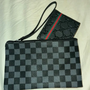 Svart rutig clutch & Gucci plånbok - Säljer en svart och grå clutch med rutigt mönster och dragkedja, samt en svart Gucci plånbok med präglade loggor och en grön-röd rand. Båda är i skinn och har stilren design, perfekt för att hålla koll på kort och cash.