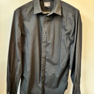 Svart slim fit skjorta från H&M - Stilren svart skjorta från H&M i slim fit-modell med klassisk krage och knappar framtill. Skjortan är tillverkad i bomull och har långa ärmar. Har blivit snyggt faded med tiden. 