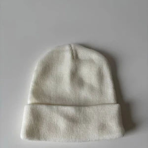 Vit stickad mössa - En stilren vit mössa med ribbad struktur och klassiskt uppvik. Perfekt för kyliga dagar och enkel att matcha med olika outfits. Mjuk och bekväm passform. Helt ny.