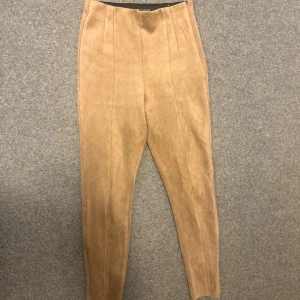 Beiga mockabyxor med hög midja - Snygga beiga byxor i mockaimitation med hög midja och avsmalnande ben. Byxorna har pressveck framtill för en clean look och är perfekta för dig som gillar en stilren och trendig vibe.