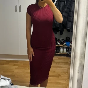 Vinröd ribbad midiklänning - Snygg vinröd ribbad klänning med kroppsnära passform och korta ärmar. Klänningen har en rund halsringning och är i midilängd, vilket ger en stilren och modern look. Perfekt för dig som gillar en enkel men chic stil. Perfekt till på julen 