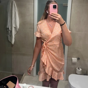 Omlottklänning med volang och knyt - Superfin kort omlottklänning i ljusorange och vitt med leopard mönster. Klänningen har volangkant nertill, korta volangärmar och knyt i midjan. Använd ett fåtal gånger☺️