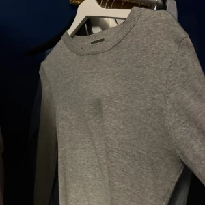 Grå stickad tröja med rund hals - En enkel och stilren grå stickad tröja med rund hals och långa ärmar. Perfekt för dig som gillar en clean look och vill ha något som funkar till jeans eller cargo. Mjuk och skön känsla tack vare det stickade materialet.