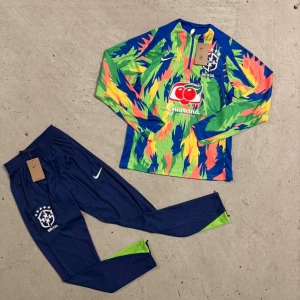 Brasilien långärmad Nike fotbollströja - Säljer en Brasilien långärmad fotbollströja från Nike med ett färgstarkt mönster i blått, grönt, gult och orange. Tröjan har tryckt landslagsmärke och sponsorlogga på bröstet. Materialet är lätt och andas, perfekt för träning eller match.