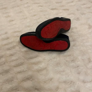 Loubs - Snygga mörkblå Louboutins i mocka med klassisk snörning och rund tå. Skorna har en unik röd sula med ingraverad text och beige innersida. Perfekta för dig som vill ha en stilren men ändå iögonfallande detalj på fötterna. Värd 9000kr med pågrund av att den är lite skadad på ena bakre delen av skon så säljes dom för 250kr. En skräddare kan sy ihop det.
