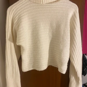 Vit ribbad polotröja från NA-KD - Säljer en vit polotröja från NA-KD i storlek L. Tröjan är ribbstickad med lång ärm och har en croppad passform. Materialet är mjukt och stickat, perfekt för att hålla dig varm under kyliga dagar. Snygg och enkel att matcha med dina favoritjeans.