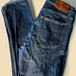 Tiger of Sweden jeans - Snygga blå jeans från Tiger of Sweden med klassisk femficksdesign, läderpatch bak i midjan och den fräna T-designen på bakfickorna. Jeansen är i modellen ”Pistolero” som är en slim fit. Kom gärna med frågor!