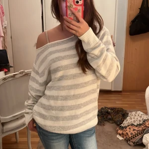 Randig stickad tröja från Subdued - Supermysig stickad tröja från Subdued med breda ljusgrå och vita ränder. Tröjan har en loose passform, bred halsringning som kan bäras offshoulder och långa ärmar med ribbade muddar. Perfekt för chill dagar och enkel att styla med jeans. Original priset är 632 kr 