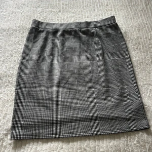 Rutig pennkjol från Cellbes - Klassisk svartvit rutig pennkjol från Cellbes i rak modell. Kjolen har elastisk midja och ett stilrent rutmönster som ger en tidlös look. Perfekt för dig som gillar en enkel men snygg stil. Längden är knälång och tyget känns mjukt och följsamt.