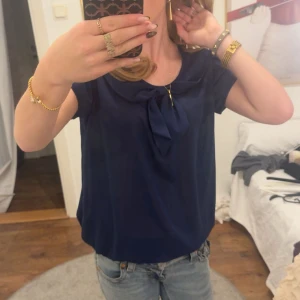 Mörkblå blus med knyt fram - Säljer en mörkblå festlig blus med korta ärmar och snygg knyt-detalj framtill vid halsen. Skitsnygg och skitskön. Säljer pga används inte. Nyskick!