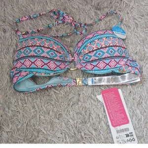 Färgglad push-up bikiniöverdel - Säljer en super push-up bikiniöverdel med snyggt geometriskt mönster i rosa, blått och svart. Den har guldfärgade detaljer, knyt i nacken och ett coolt spänne i ryggen. Perfekt för dig som vill ha extra stöd och en färgstark look på stranden!