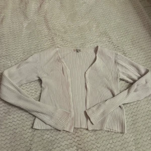 Vit ribbad kofta från SAMSA - Säljer en vit ribbad kofta från SAMSA Young. Koftan har lång ärm, kort i magen, v-ringning och knappar framtill. Den är i ett mjukt, stretchigt material och har en clean, enkel look som passar perfekt till jeans eller kjol.