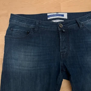 Jacob Cohen nick, storlek 35, 10/10 skick - Mörkblå jeans från Jacob Cohën i klassisk femficksmodell. Modellen är nick och storleken är w35. Snygga detaljer som knappar och patch. Tillverkade i Italien  i mjukt denimtyg som sitter skönt hela dagen. Nypris är ca 5000 SEK. Säljer då de inte passar mig. Använda ett fåtal gånger, mycket bra skick 10/10