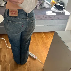 Levi's 514 blå jeans straight fit - Säljer ett par klassiska Levi's 514 jeans i blå denim. Modellen har rak passform, låg midja. Jeansen har slitningar och hål på ena knät för en cool, avslappnad look. Perfekta för dig som gillar vintagekänsla och tidlös stil. Andvända men inga slitningar mer än vad modellen är, exempelvis hålet i knäet. 