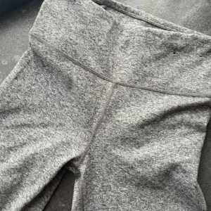 Gråa höga leggings i mjukt material - Säljer ett par gråmelerade leggings med hög midja. De är tillverkade i ett mjukt och stretchigt material som sitter tight och bekvämt. Perfekta för träning eller chill dagar. Snygg sömdetalj framtill för extra stilpoäng.