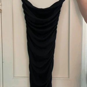 Svart långklänning från Amisu - Snygg svart långklänning från Amisu med draperad effekt längs hela klänningen. Klänningen har en figurnära passform och är ärmlös med en stilren, enkel design. Perfekt för dig som vill ha en elegant och tidlös look.