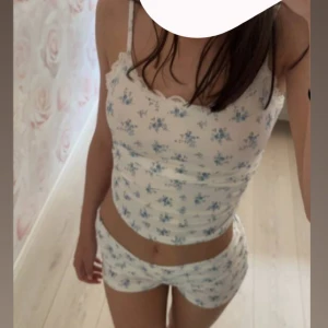 Vit blommig pyjamas set i silke - Säljer en söt vit blå blommig pyjamas set med spetsdetaljer längs halsringningen på linnet. Väldigt stretchigt och silkes material , och linnet går att justera banden på i bak✨Linnet är lite använd men byxorna är endast testade