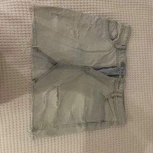 Ljusblå jeansshorts från Zara - Säljer ett par ljusblå jeansshorts från Zara med råa kanter och slitna detaljer både fram och bak. Shortsen har klassisk femficksdesign, bälteshällor och dragkedja. Perfekta för en chill sommarlook. Andvänd några gånger men inget man ser. Köpt för: 390kr 
