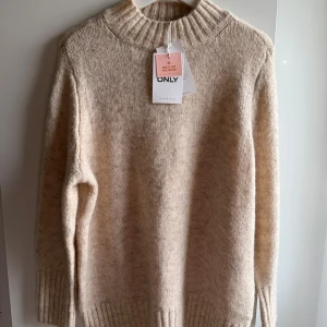 Ny Only beige tröja, storlek L - •Mysig beige stickad tröja från ONLY med ribbad hög krage och breda muddar vid ärmslut och nederkant.  •Tröjan har en avslappnad passform och clean look,  perfekt för lager-på-lager och chill vibes.  •Tillverkad i en mjuk blandning med återvunnen polyester.