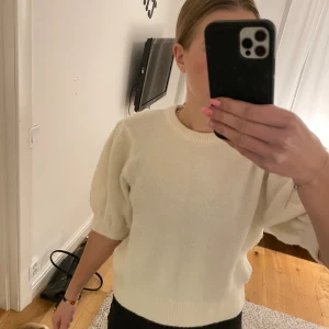 Krämvit stickad tröja med puffärm - Superfin krämvit stickad tröja med puffiga, halvlånga ärmar och rund halsringning. Tröjan har en mjuk och mysig känsla och ribbade muddar vid ärmslut och nederkant. Enkel att styla till jeans eller kjol. Nyskick, säljer då jag rensar ut garderoben