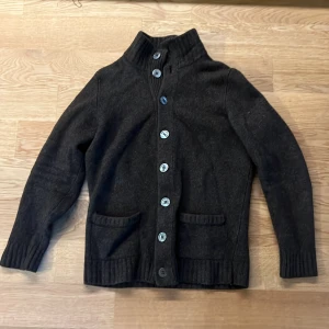 Mörkbrun kofta från Alan Paine - Säljer en mörkbrun kofta från Alan Paine med hög krage och knappar hela vägen framtill. Koftan är stickad i ull och har två fickor framtill. Varan passar längd 170 ungefär. Perfekt nu för vintern då den är riktigt varm 🤩 