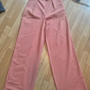 Vida rosa byxor från ASOS 32 - Snygga vida byxor från ASOS i en dämpad rosa färg. Byxorna har hög midja, raka ben.  Perfekta för dig som gillar en trendig och avslappnad look.