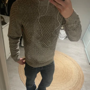 Stickad tröja  - Säljer en grå stickad tröja från Kappahl med snyggt strukturmönster och rund hals. Tröjan har långa ärmar och ribbade muddar vid ärmslut och nederkant. Perfekt för kyliga dagar. Nypris 600 aldrig använd. 