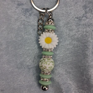 Nyckelring med pärlor och blomma - Superfin nyckelring med silikonpärlor i mintgrönt,vitt och glittriga mellandelar. dekorerad med en vit prästkrage/tusensköna.  Perfekt att hänga på väskan eller nycklarna för en söt touch.