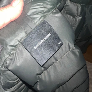 Svart dunjacka från Peak Performance - Säljer en mörkgrön dunjacka från Peak Performance med huva och dragkedja. Jackan är quiltad och har en clean, sportig look med ribbade muddar vid ärmslut och nederkant. Perfekt för kalla dagar och riktigt snygg till streetwear-stilen.