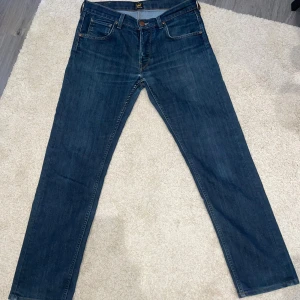 Lee Daren jeans W31 L32 blå - Säljer ett par klassiska Lee Daren jeans i mörkblå denim. Modellen har raka ben, fem fickor och snygga kontrastsömmar. Jeansen har Lee-logga på bakfickan och är tillverkade i bomullsjeans. Perfekta för dig som gillar en tidlös look.