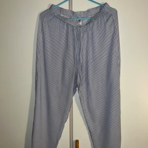 Pyjamasbyxor från Lindex - Snygga och luftiga linnebyxor från Lindex i storlek S. Byxorna har ett blåvitt randigt mönster, elastisk midja och avslappnad passform. Perfekta för dig som gillar chill och stilren look. Materialet är mjukt linne som känns skönt mot huden.