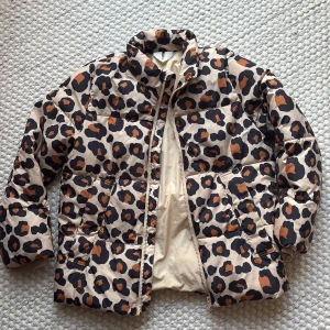 Leopardmönstrad pufferjacka från ARKET - barn - Säljer en beige pufferjacka från ARKET med coolt leopardmönster i svart och brunt. Jackan har hög krage, två fickor fram och dragkedja. Storlek 134-140, passar både tjej och kille. 