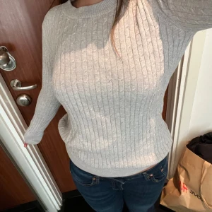 Ljusgrå stickad tröja Gina Tricot - Superskön ljusgrå stickad tröja från Gina Tricot med klassiskt kabelstickat mönster. Perfekt att slänga på sig när det är kyligt ute.