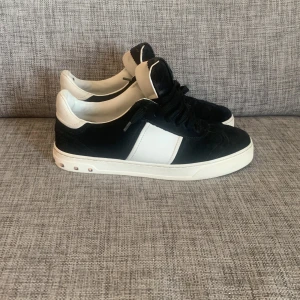 Valentino Flycrew - Svarta och vita Valentino Rockstud sneakers i mocka och skinn med klassiska nitar på hälen. Snygg kontrast mellan svart ovandel och vita detaljer, samt cool sula med mönster undertill. Perfekta för dig som gillar exklusiva och trendiga sneakers. Priset går att diskutera vid en snabb affär