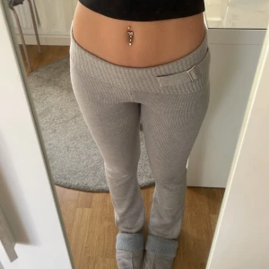 Grå ribbade stickade byxor - Säljer ett par grå ribbade stickade byxor med bred midja och snyggt bältdetalj framtill. Byxorna  är mjuka. Modellen är figurnära upptill och vidare nertill. Använt en gång.