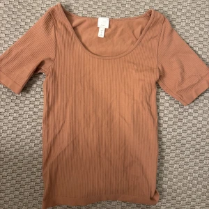 Ribbad brun topp från H&M XS - Säljer en ribbad brun topp från H&M i storlek XS. Toppen har rund halsringning och korta ärmar. Materialet är mjukt och stretchigt, perfekt för en chill och enkel look. Passar dig som gillar basic och stilrena plagg.