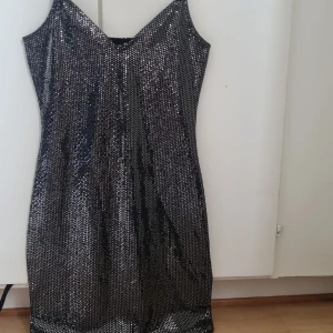 Glittrig silverklänning från H&M Divided - Säljer en snygg glittrig klänning från H&M Divided i storlek XS. Klänningen är lång, ärmlös och har en cool silverfärgad paljettlook som verkligen sticker ut. Perfekt för dig som vill glänsa och synas med en trendig och festlig stil.