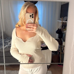 Ribbad beige långärmad tröja - Säljer en beige ribbad långärmad tröja med v-ringad hals och coola slitsar vid ärmsluten. Tröjan har en mjuk och stretchig känsla, perfekt för dig som gillar en enkel men snygg look. Passar dig som vill ha en neutral färg och stilren design. Storlek XL men passar mig som brukar ha S/M