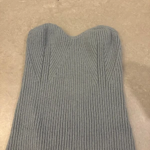 Grå ribbad axelbandslös klänning - Säljer en snygg grå axelbandslös klänning i ribbstickat material. Toppen har en figurnära passform och markerad byst, perfekt för dig som gillar minimalistisk och stilren design. Enkel att styla med smycken eller boots för en cool look.