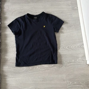 Mörkblå t-shirt från Lyle & Scott - Snygg mörkblå t-shirt från Lyle & Scott med klassisk gul logga broderad på bröstet. T-shirten har rund halsringning och är tillverkad i mjuk bomull. Perfekt basic-plagg med stilren look.