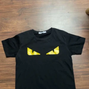 Fendi T-shirt  - Cool svart t-shirt från CityFash med ett unikt tryck av gula ögon på bröstet. T-shirten har rund hals och korta ärmar, perfekt för dig som gillar att sticka ut med grafiska detaljer. Materialet känns mjukt och skönt mot huden.